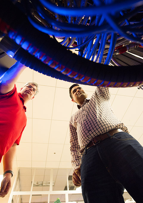 Two men stand above a bunch of wires. 